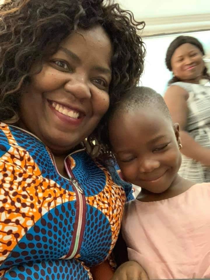 A mother in vibrant Ankara-style clothing takes a warm selfie with her young daughter
