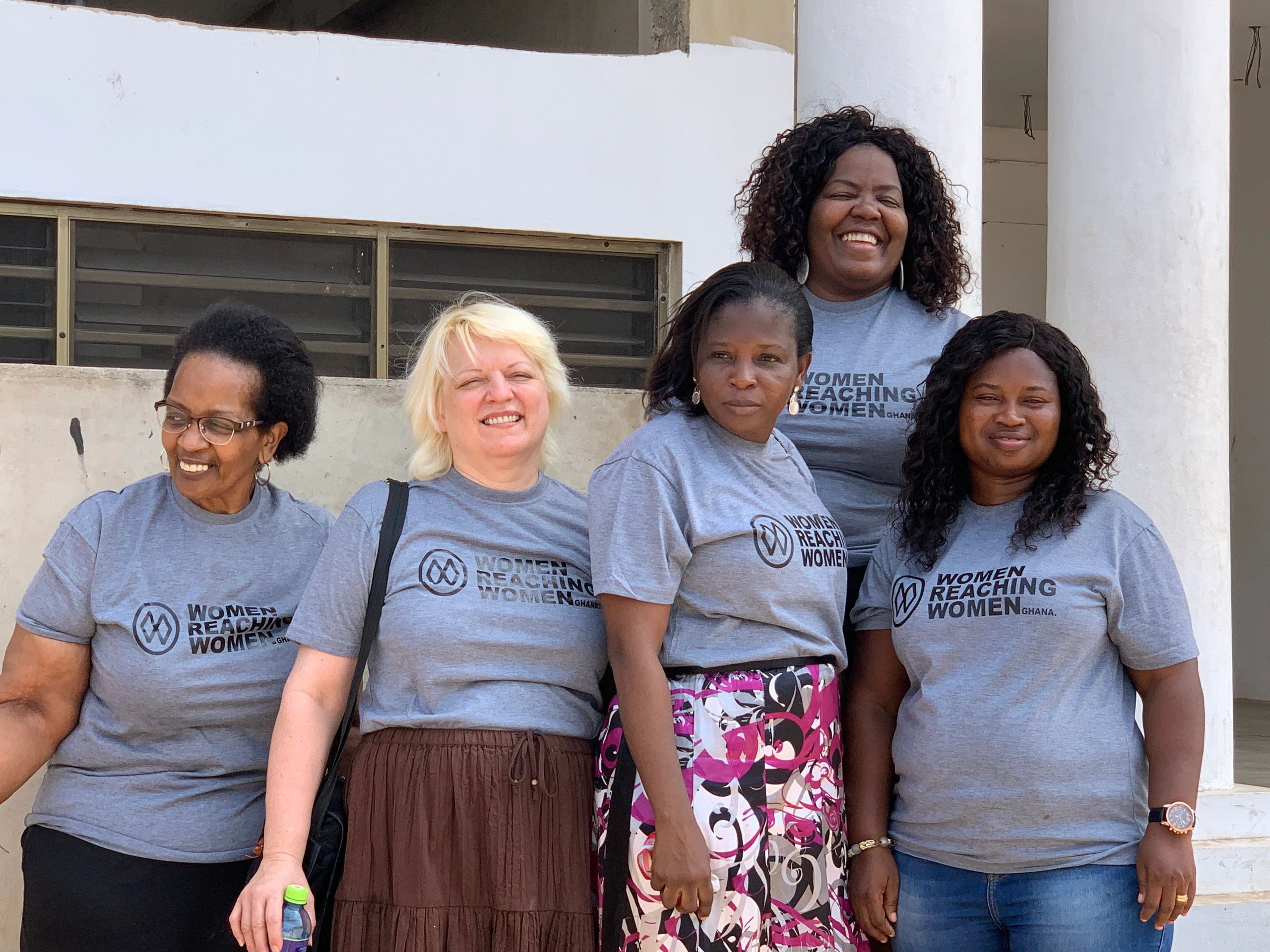The Women Reaching Women Ghana team in matching shirts outside a white building with columns